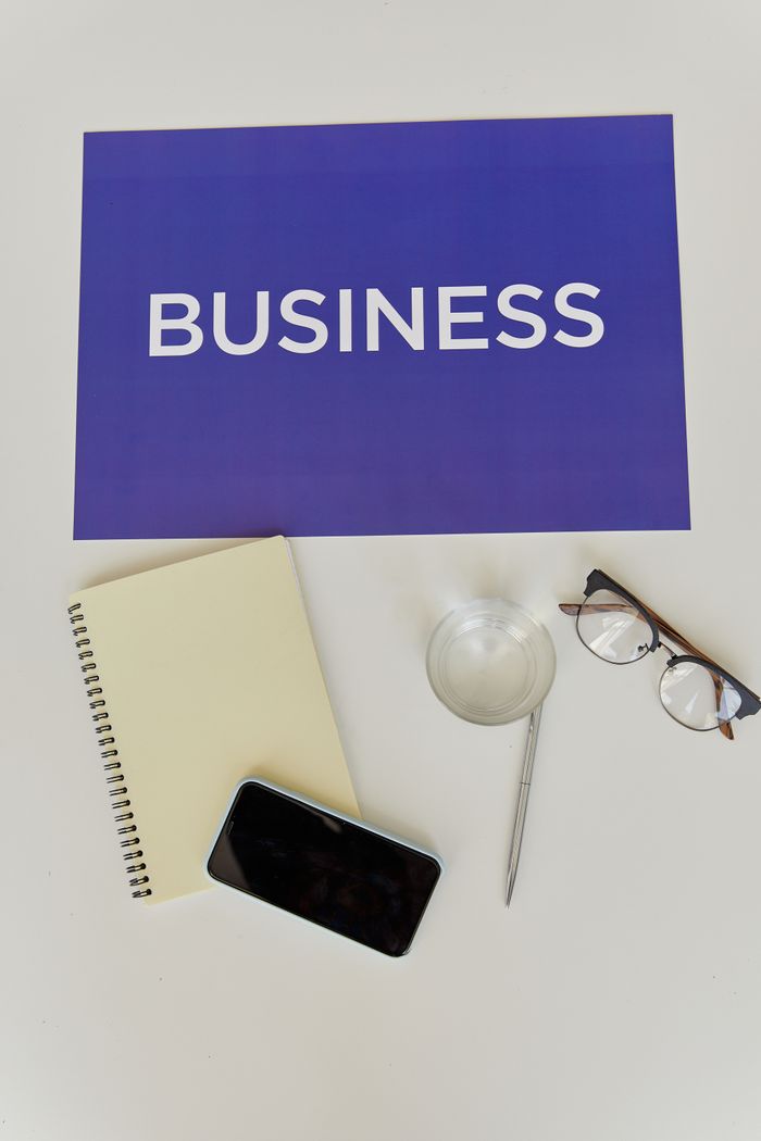 A business-themed flat lay with essentials like a notebook, smartphone, glasses, and a sign.